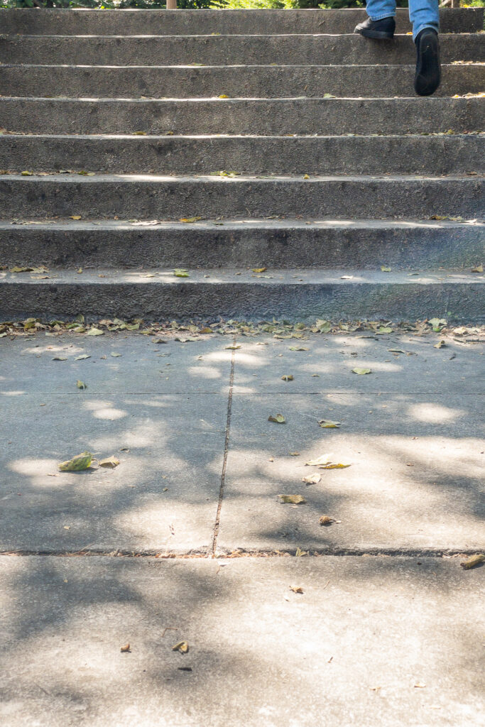 Photograph;  a walkway leading to a short set of stairs with a person feet reaching the top.