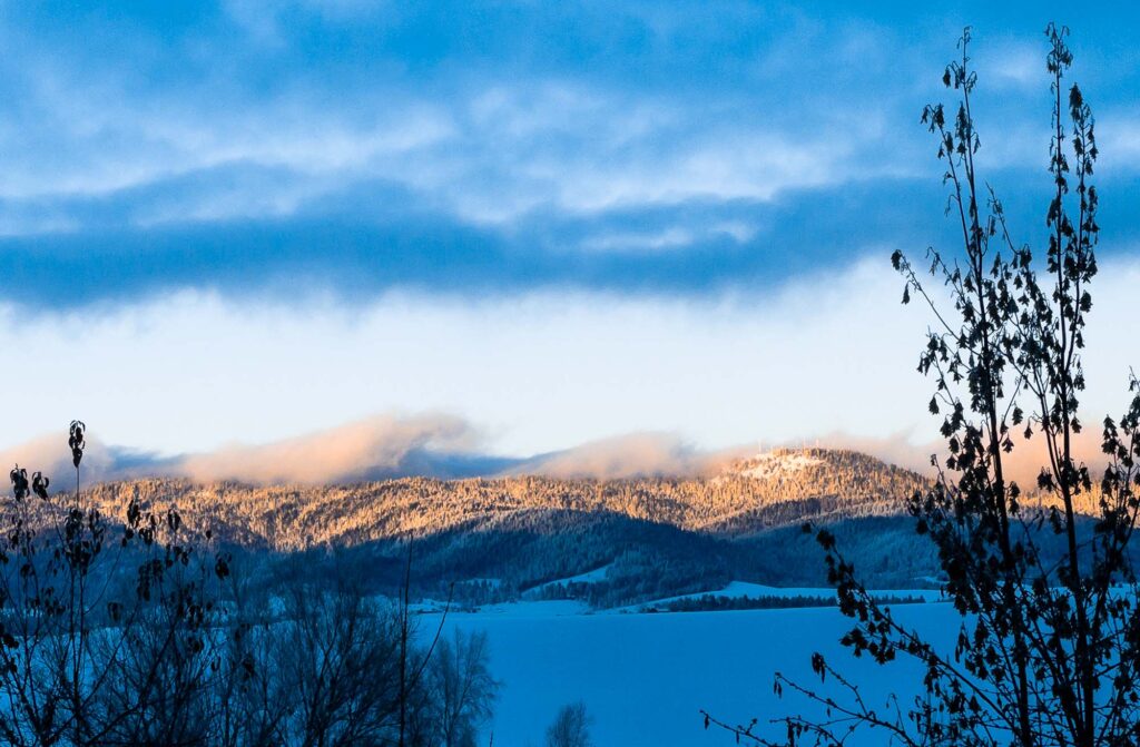 Photograph; Moscow mountain covered in winter evening sunshine, snow, and wavy clouds along its peak.