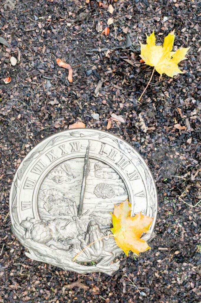 Photograph of a sundial and two fallen yellow leaves on an foggy day in early autumn.