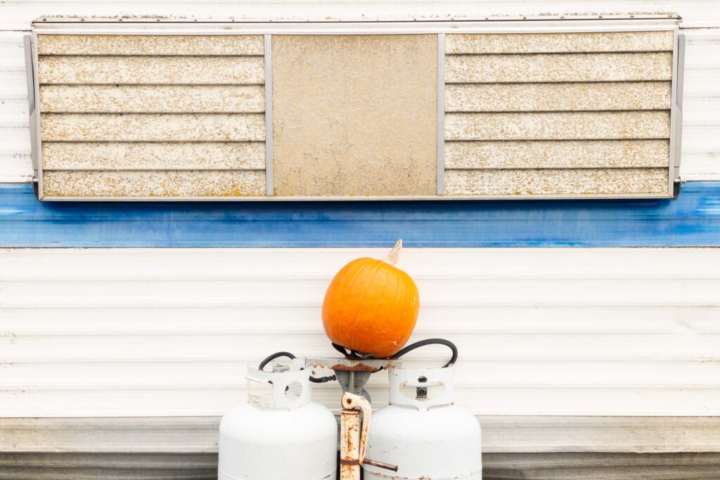 Photograph; an uncarved pumpkin on top of two propane tanks on the front of an old travel trailer.