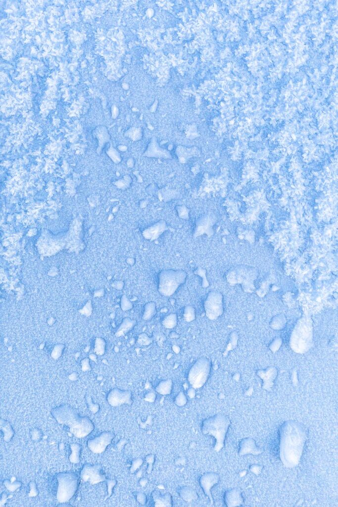 Photograph; frozen rain and snow on the hood of a blue car at dawn. 