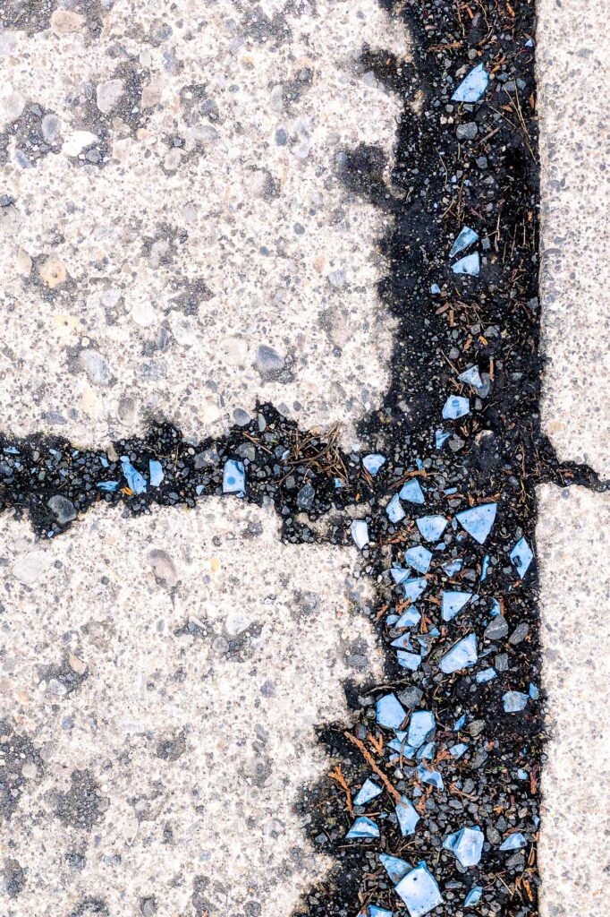 Photograph of cracks in a driveway filled with mud and broken pieces of blue ceramics.