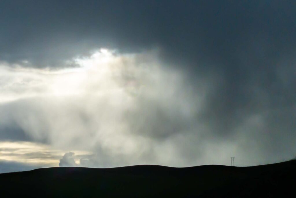 Photograph of spring clouds and rain over clearing over the Palouse hills with a lone power pole. 