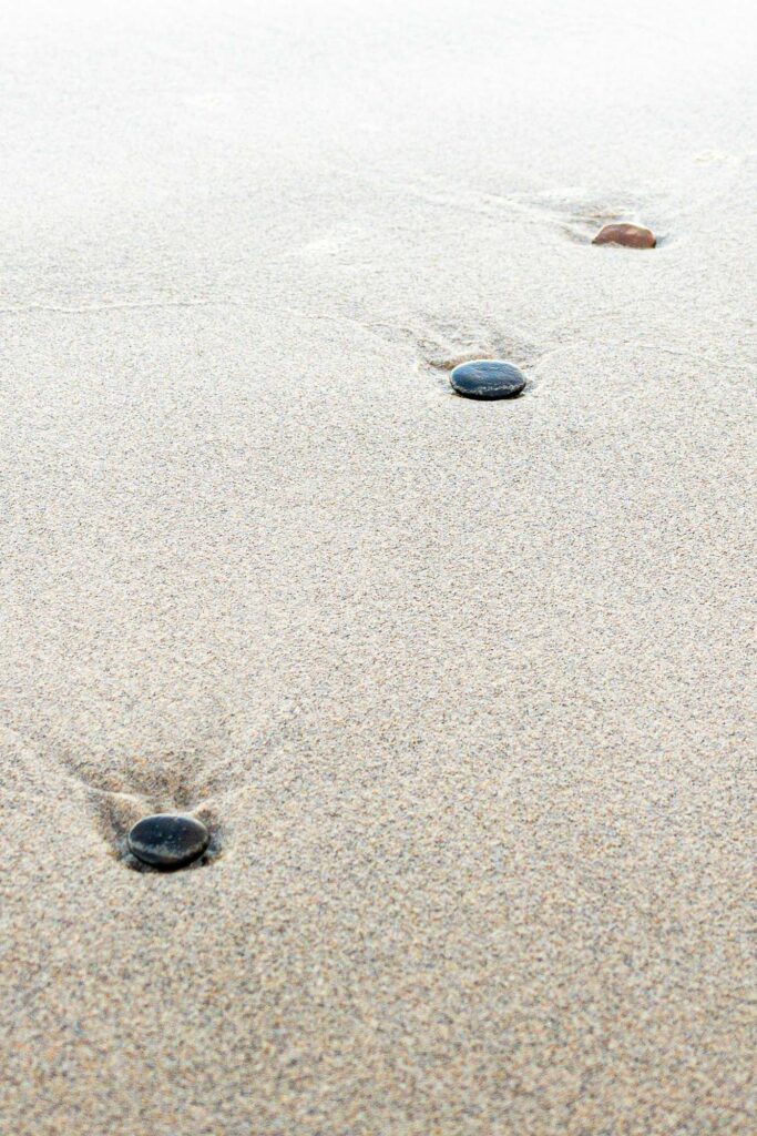 Photographs of stones on a beach in a diagonal pattern, sunk in the sand after receding ocean wave.