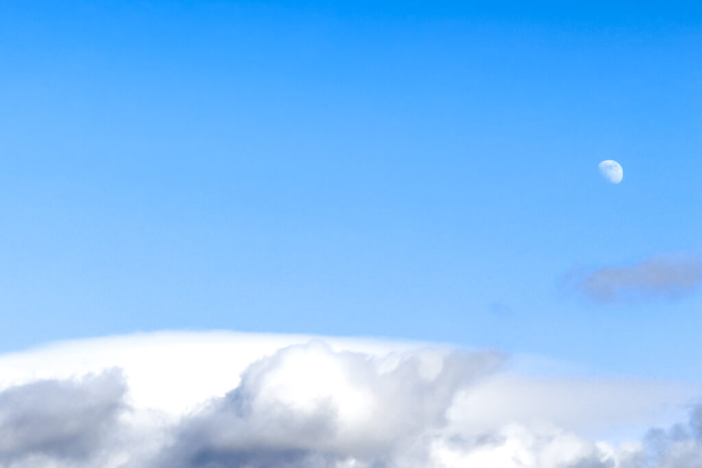 a waxing quarter moon above a cloud sculpted by the wind.