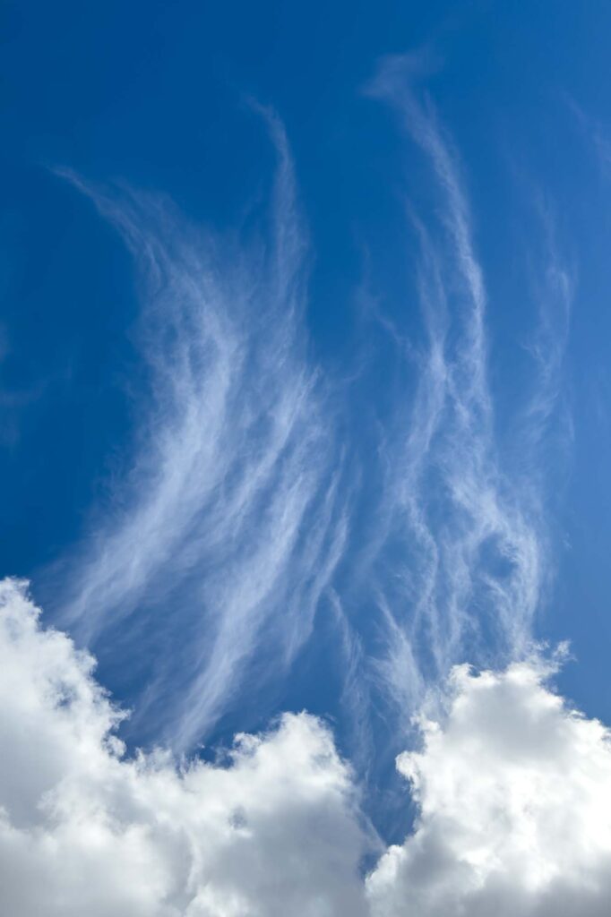 Portrait photograph with wispy clouds rising from thick clouds into a deep blue sky