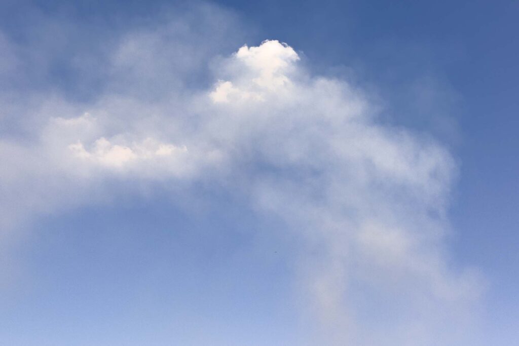 Color photograph of dust rising high in the sky forming clouds. The dust is rising from a field being plowed (or cultivated) and seeded.