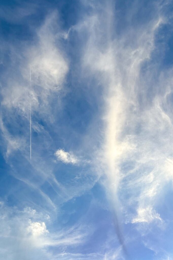 Coloring photograph of high cirrus clouds in the glow of the setting sun. In the clouds on the left, a plane and its contrail.