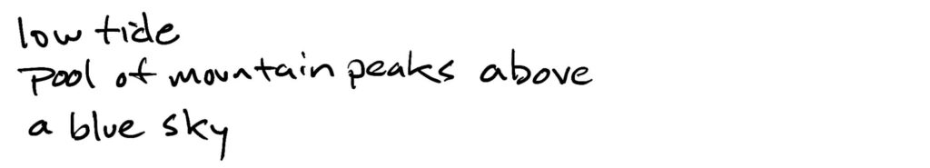 low tide/pool of mountain peaks above/a blue sky