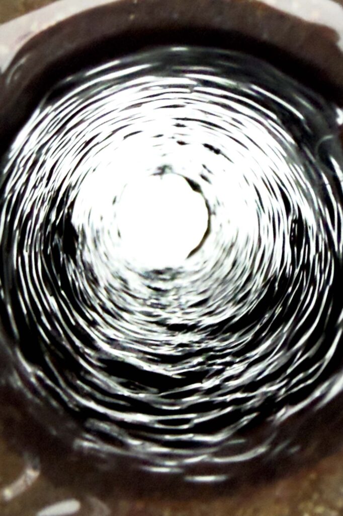 Color photograph of a drain pipe emptying out into white space .